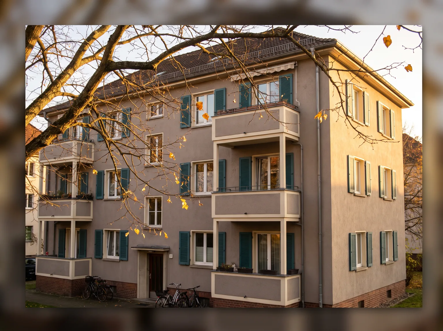 Dreigeschossiges Mehrfamilienhaus mit Balkonen, durch herbstliche Zweige gesehen.